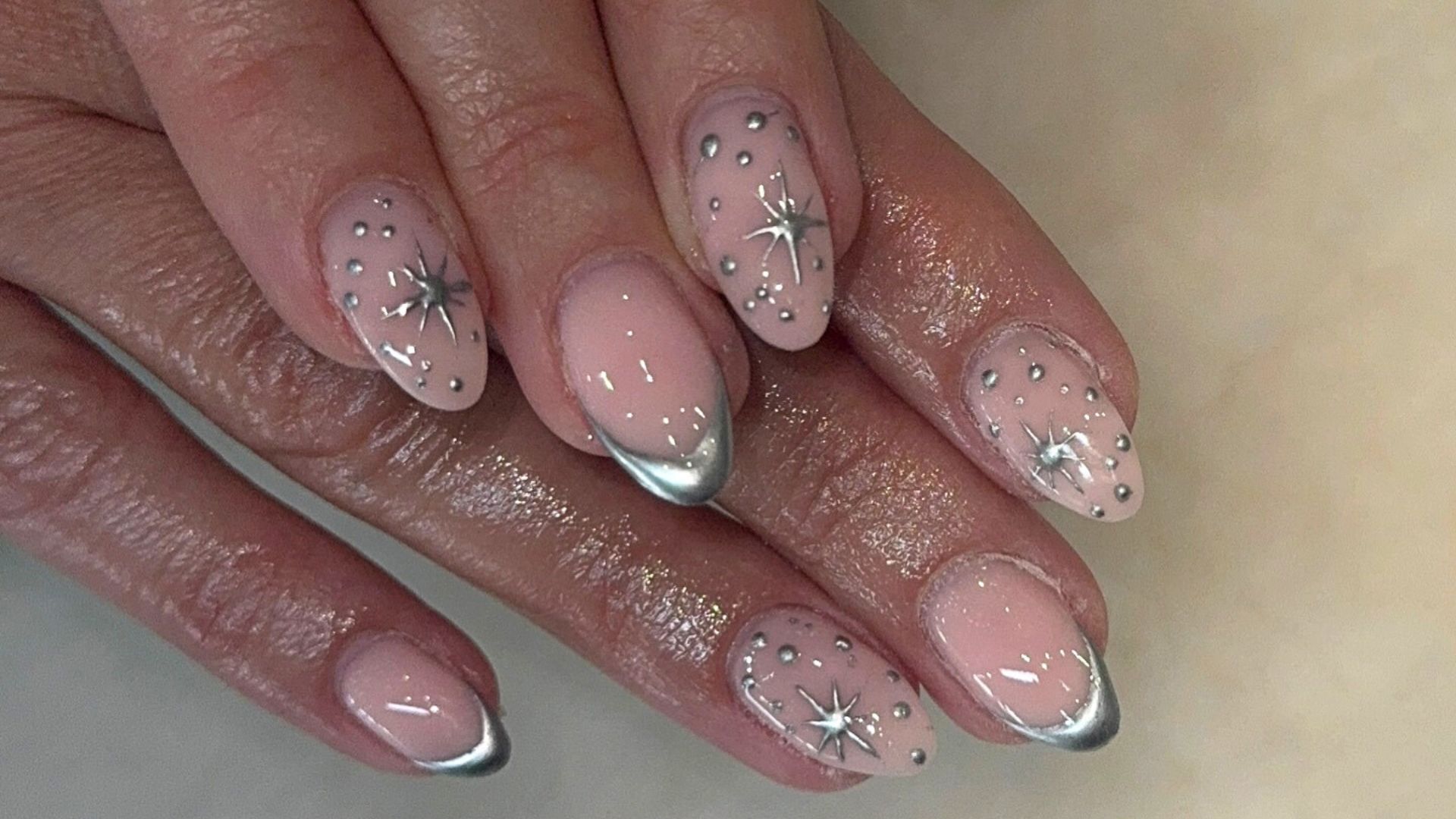 A close-up of hands with almond-shaped nails painted in pink, featuring silver tips, delicate silver studs, and star-shaped designs—ideal for summer nail designs and anyone who loves on-trend nails.
