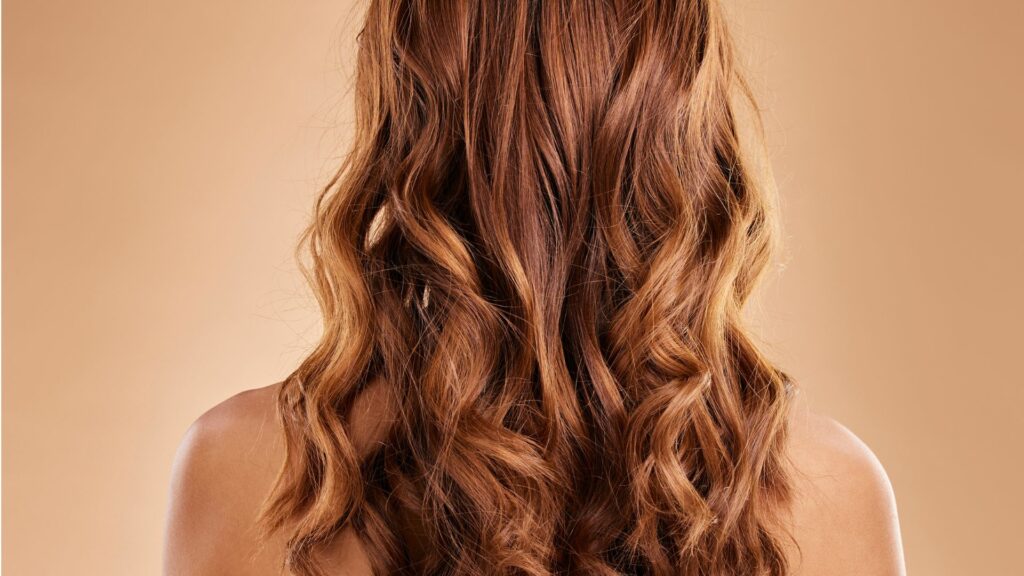 A person with long, wavy, light brown hair is seen from behind against a light beige background, creating a sense of calm and stress relief.
