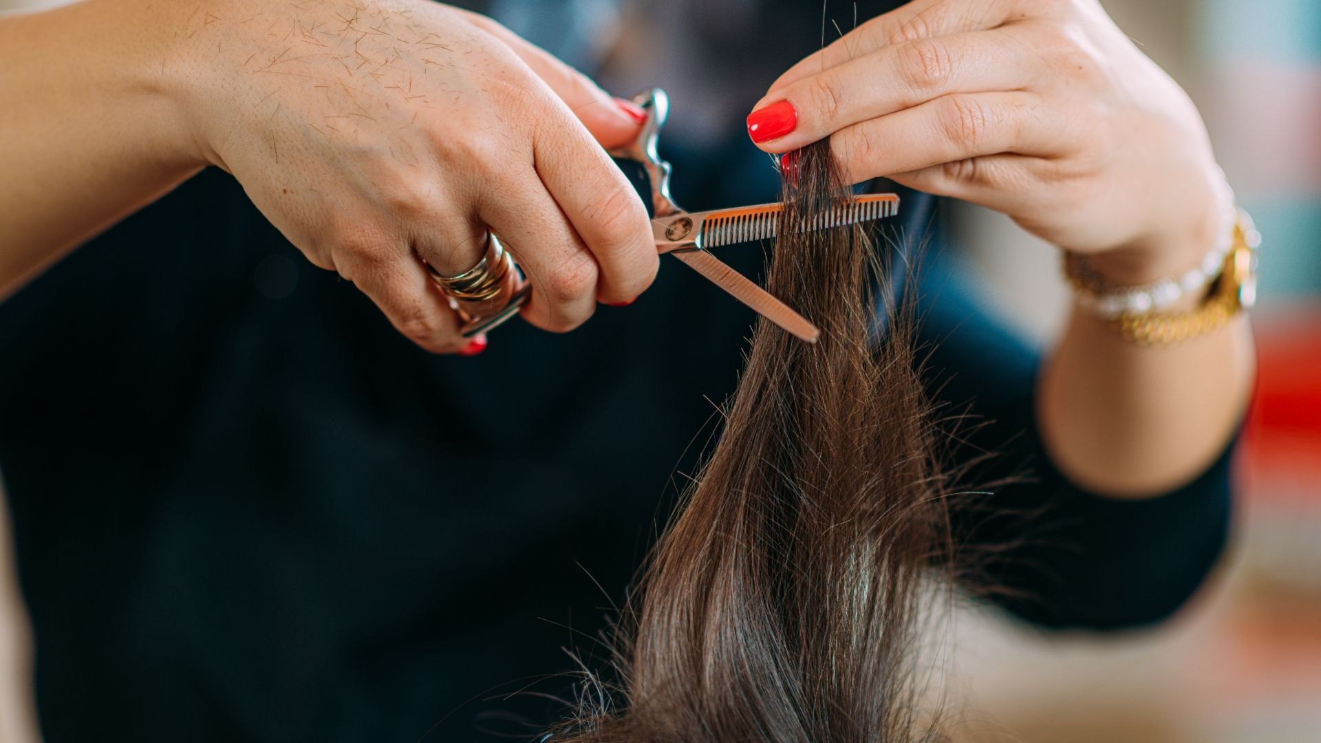 Someone with red nail varnish trims a section of brown hair with scissors, highlighting one of the leading Healthy Hair Tips for keeping hair glossy and in good condition.