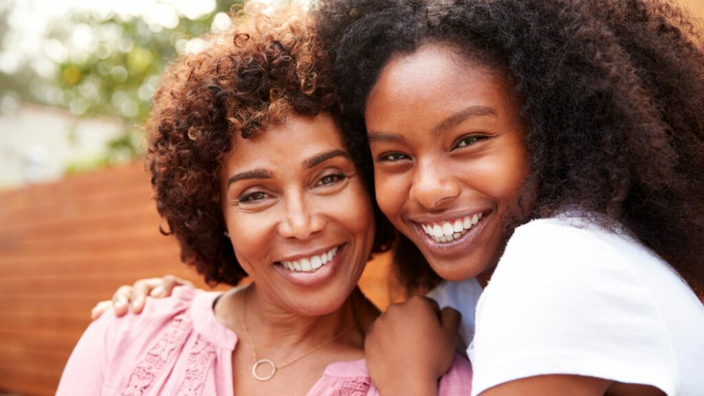 Two women smiling and standing close together outdoors, one wearing a pink top and the other in white—a touching moment ideal for a Mother’s Day present or to mark Mother’s Day.