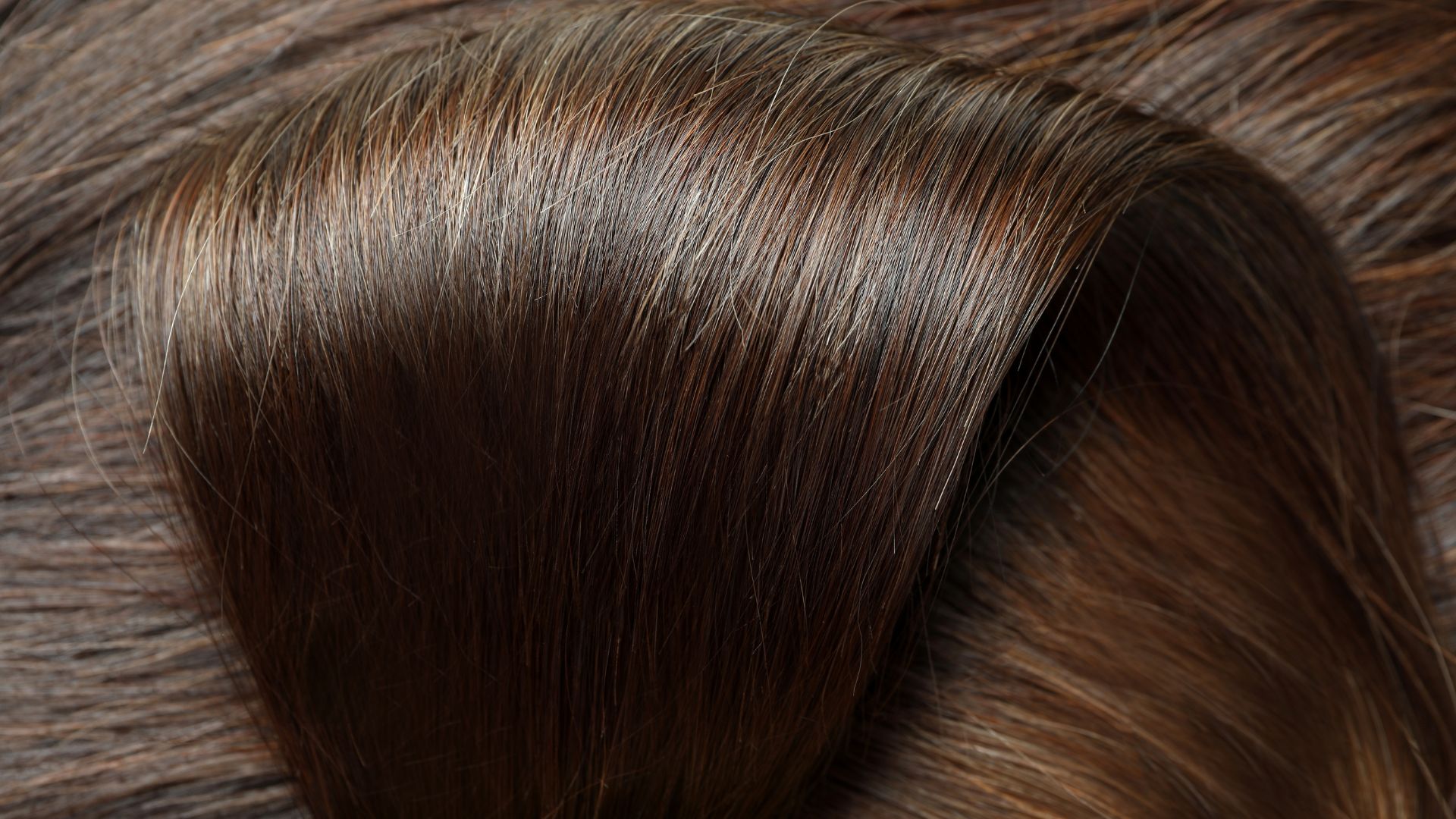 Close-up of sleek, glossy, dark brown hair with natural highlights, displaying a healthy texture and shine under the light following an indulgent Kérastase Salon treatment.