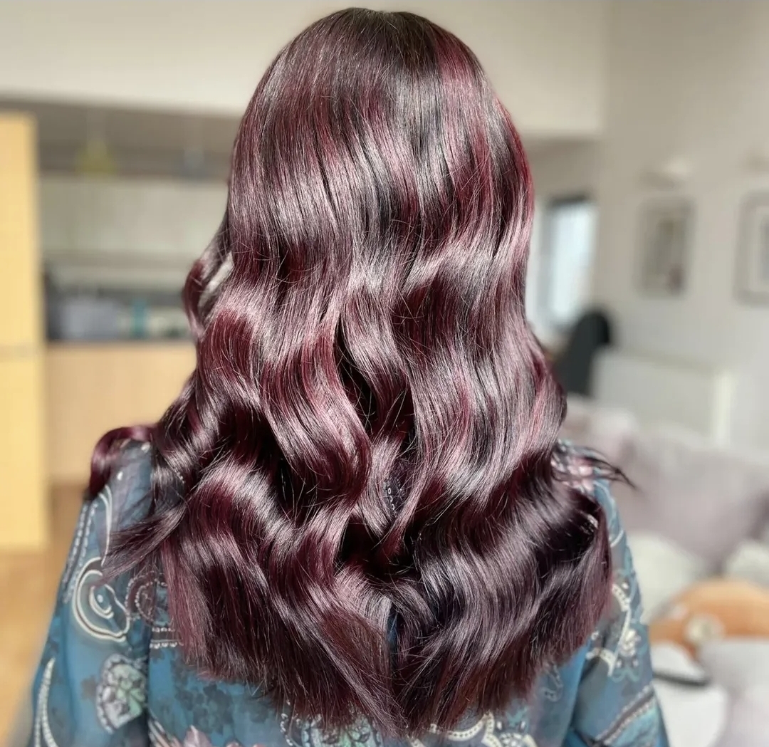 An individual with long, wavy, dark burgundy hair is seen from behind, indoors in a brightly lit room following a hair treatment session in Widnes.