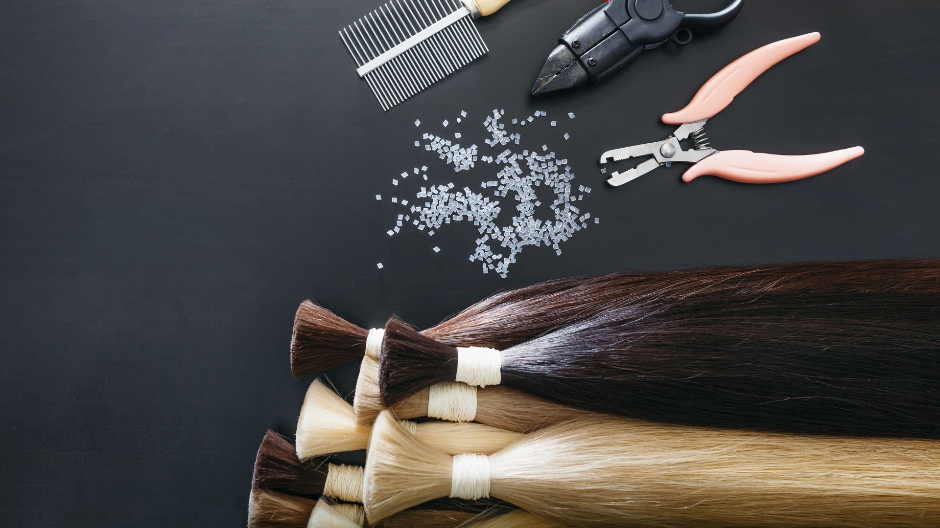 Bundles of hair extensions, combs, pliers and small beads are neatly laid out on a black surface, presenting a hair styling arrangement that emphasises salon efficiency.