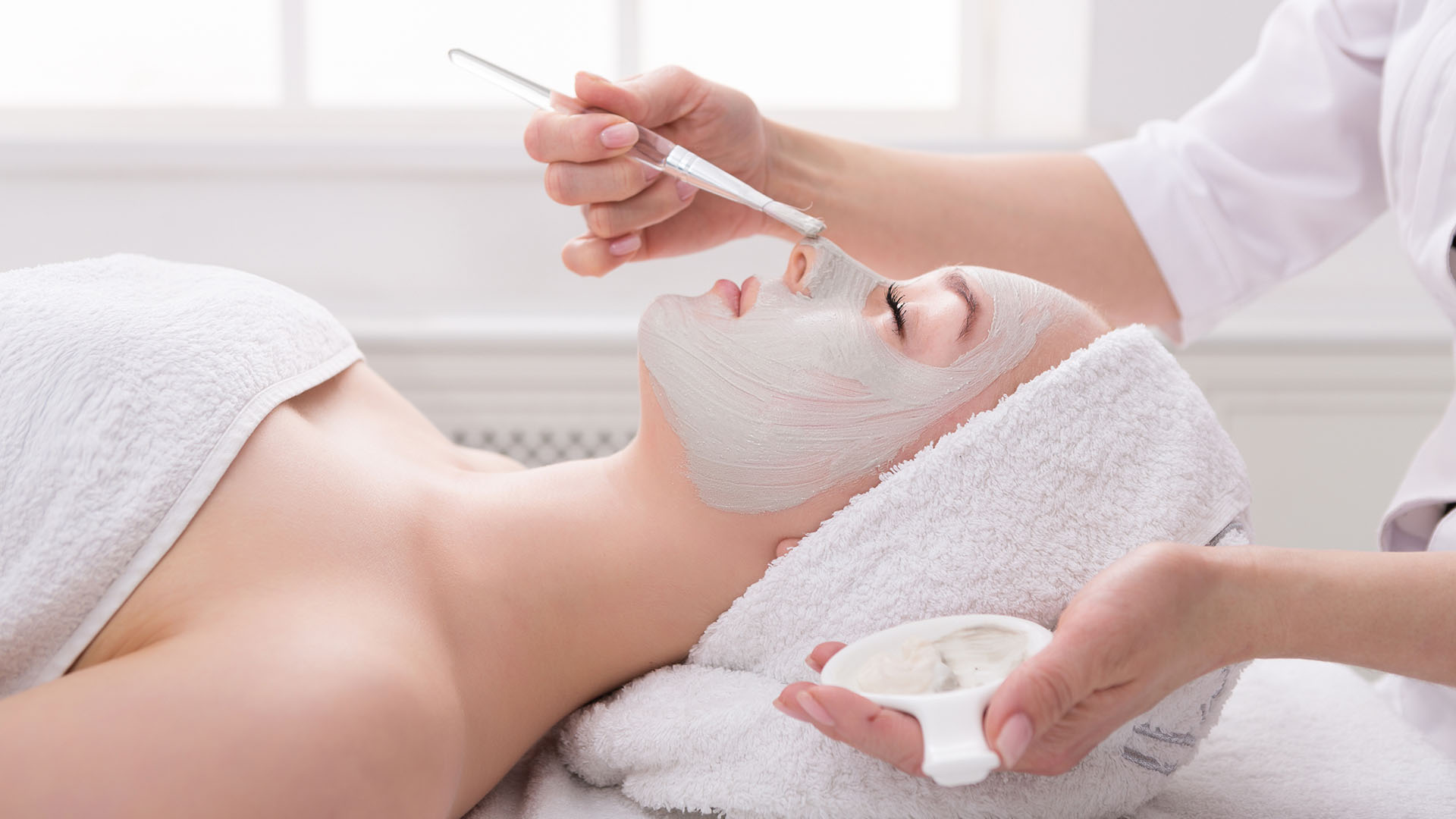 A person relaxes on a spa bed with their hair wrapped in a towel, enjoying a rejuvenating facial mask—ideal for your skincare routine this autumn.
