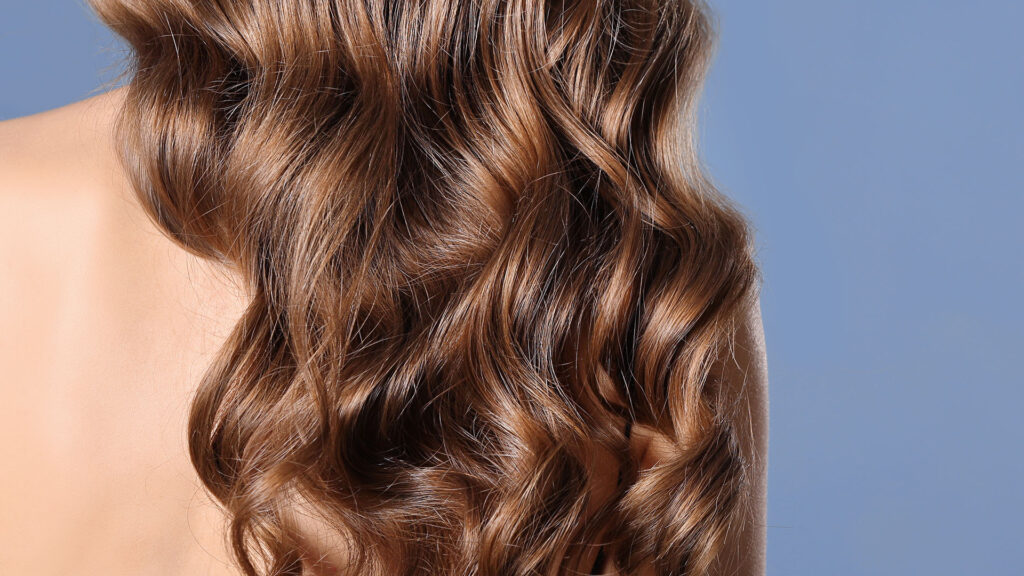 Long, wavy brown hair styled in a modern perm trend 2026 look, falling over a person’s shoulder.