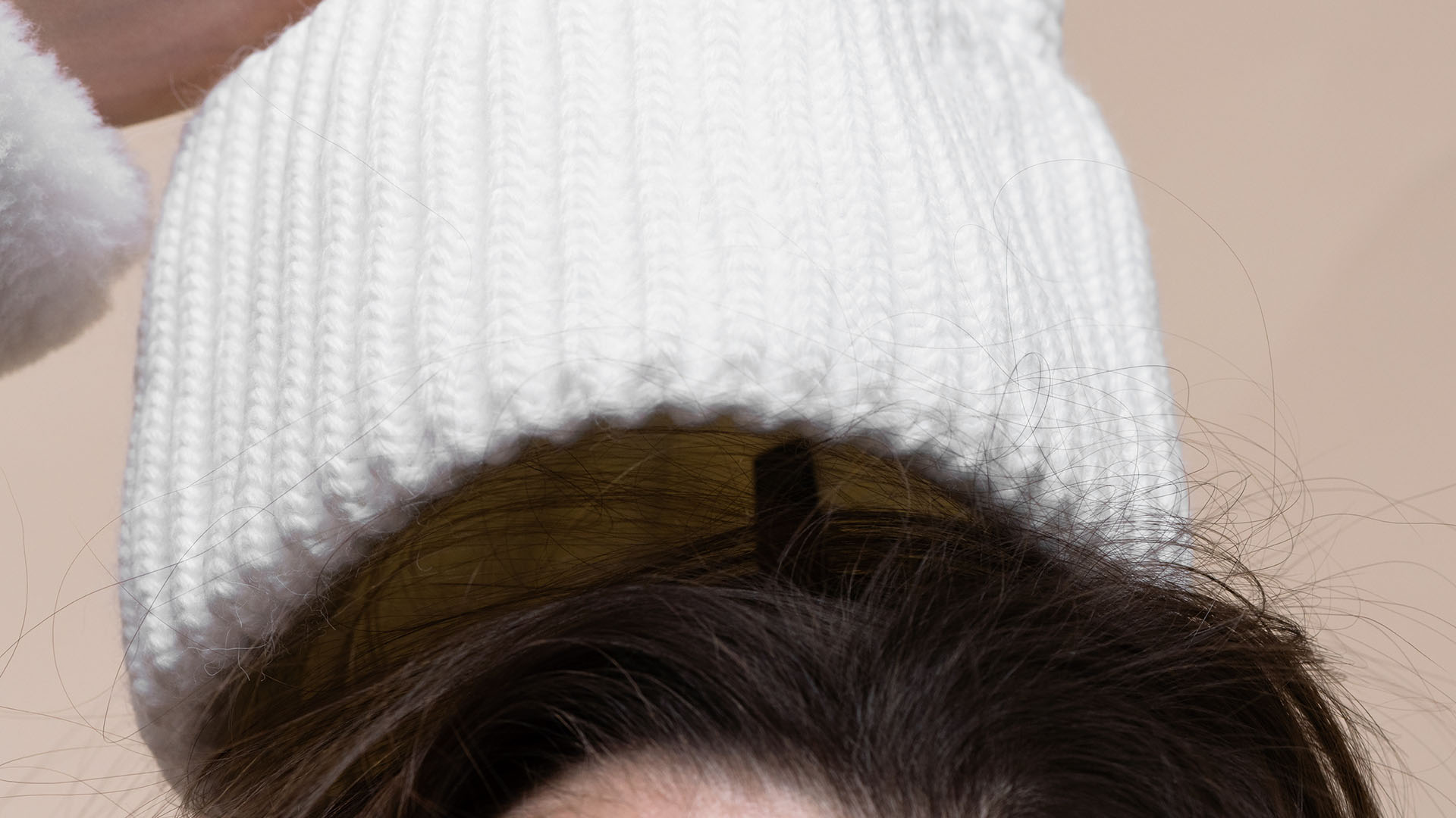 A person wearing a white ribbed-knit beanie to manage hat hair.